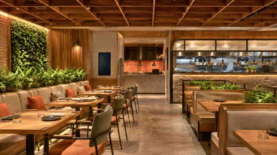 Restaurant dining area with a living green wall, potted plants, and an open kitchen in the background